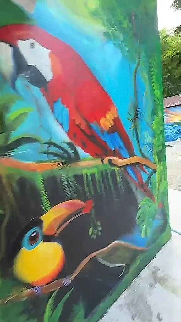 Mural de una lapa roja y un tucán entre la selva